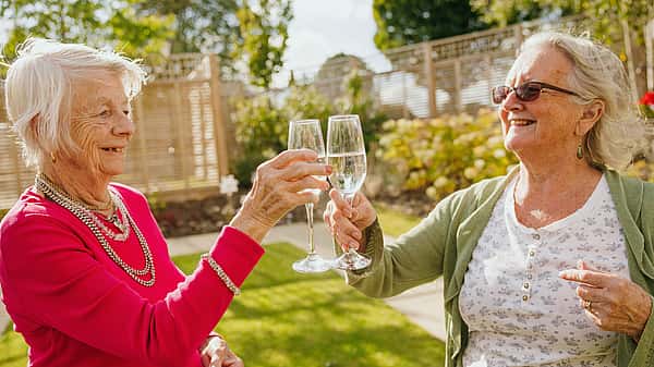 Two elderly women toasting with glasses of champagne in a garden