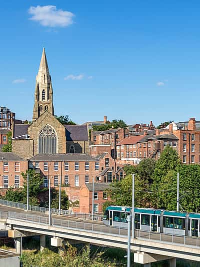 A modern tram gliding through an elevated track, with a backdrop of historic buildings and church towers in Nottingham.