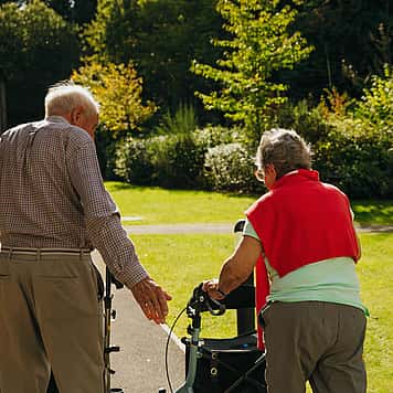 A picture of two elderly couple from behind, taking a walk with the aid of a walker