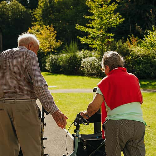A picture of two elderly couple from behind, taking a walk with the aid of a walker