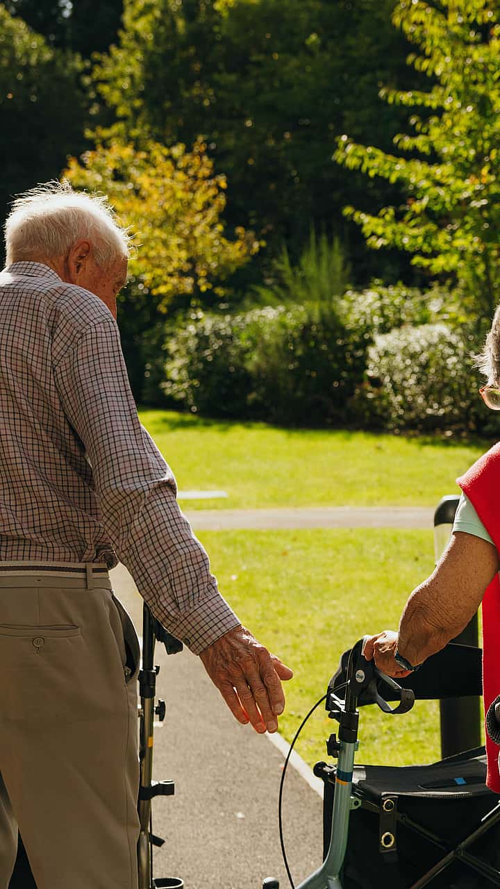 A picture of two elderly couple from behind, taking a walk with the aid of a walker