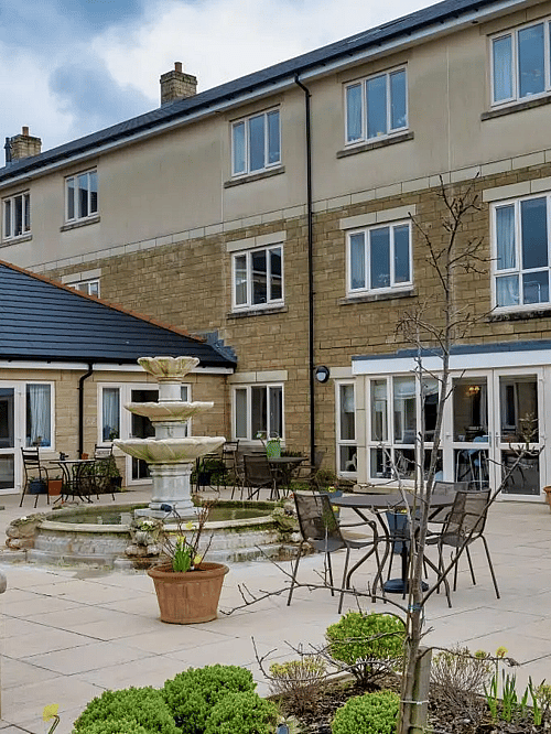 A peaceful courtyard with a fountain, surrounded by seating areas and a building in the background.