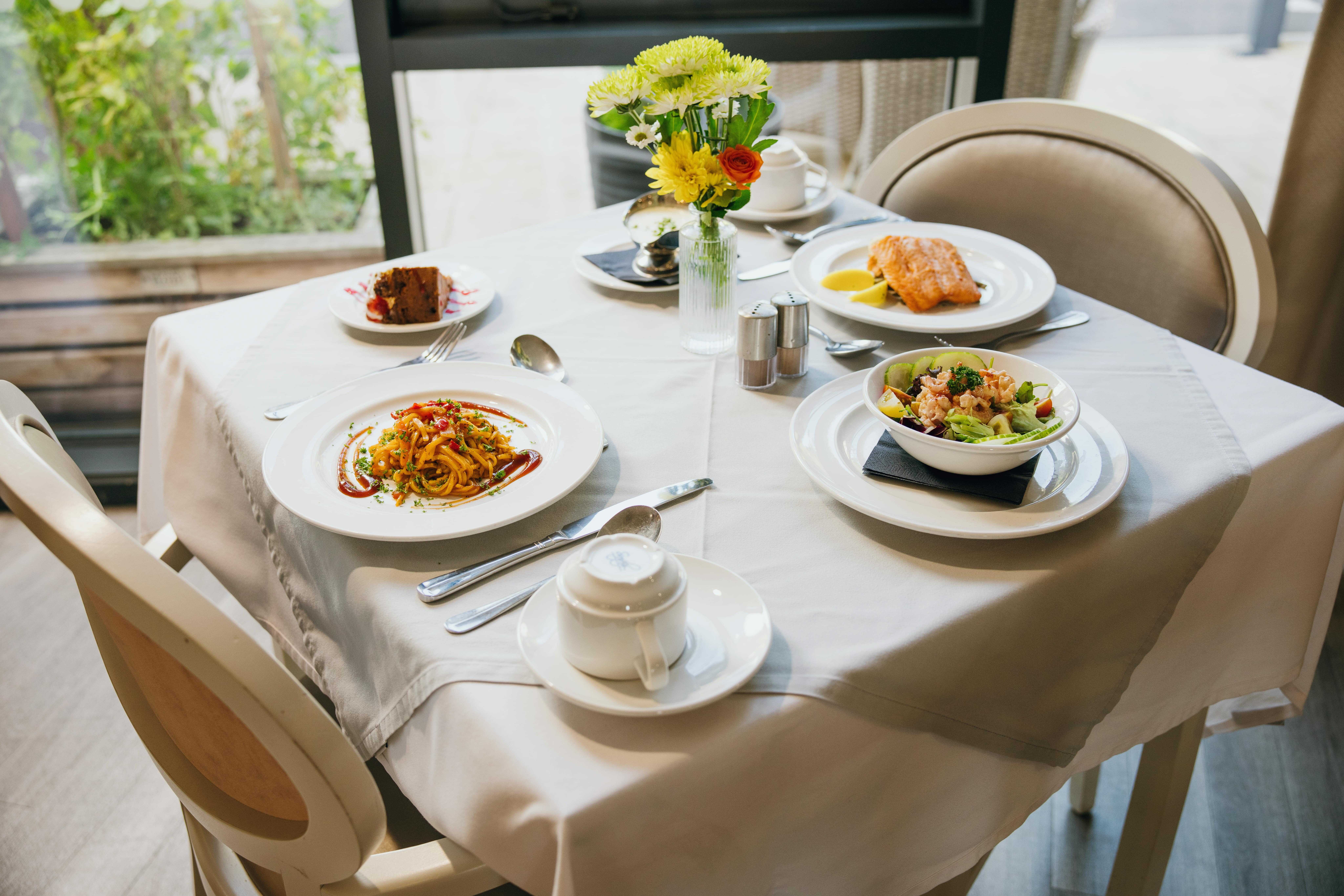 A table setting with a meal for two individuals along with vase of flowers