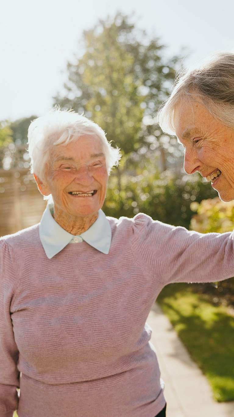 Two elderly women are happily walking and chatting together outdoors on a sunny day