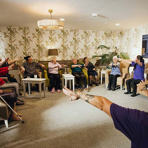 Care professionals conducting an exercise class with a group of elderly individuals in attendance