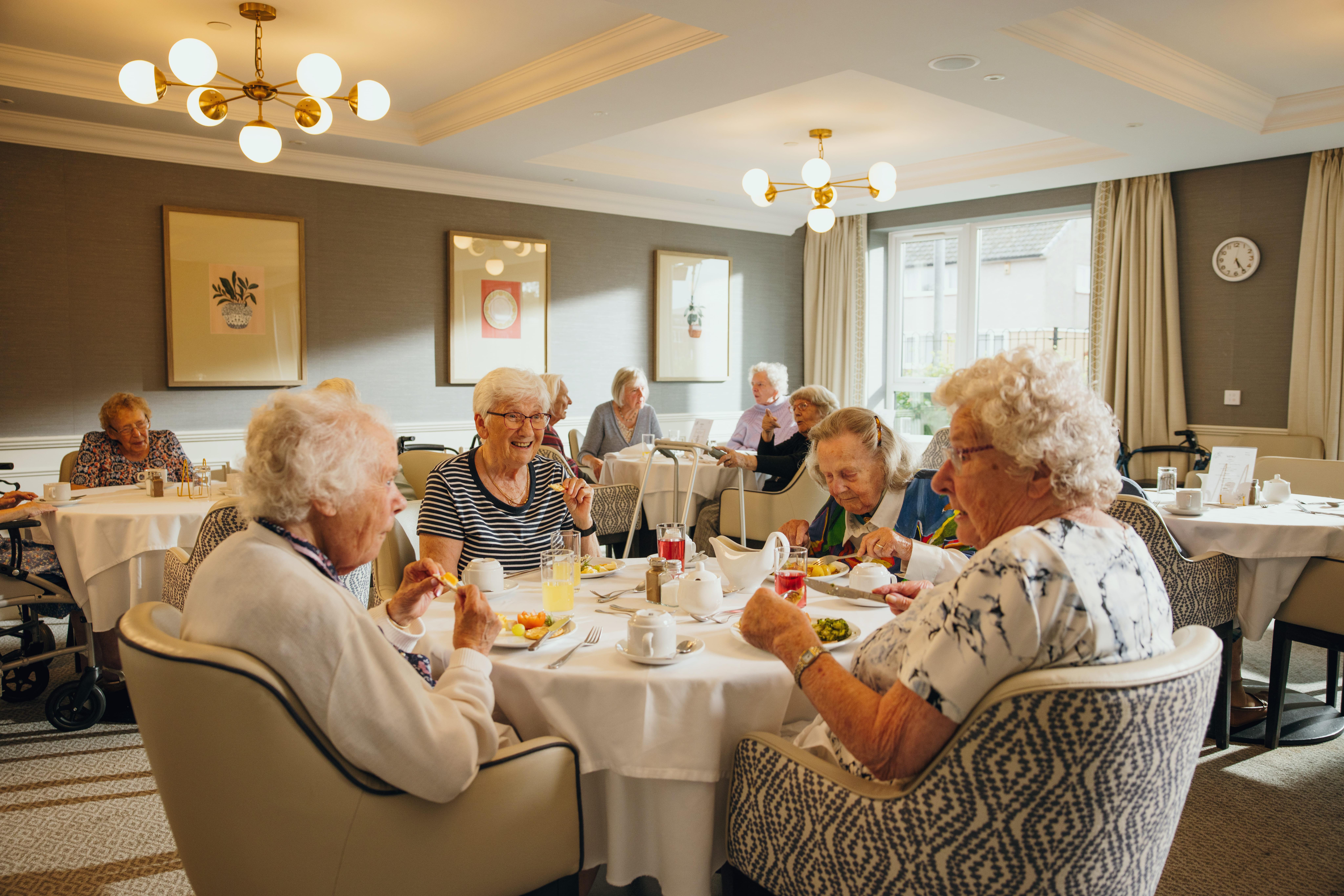 A group of elderly people are enjoying a meal together in a warmly lit dining room