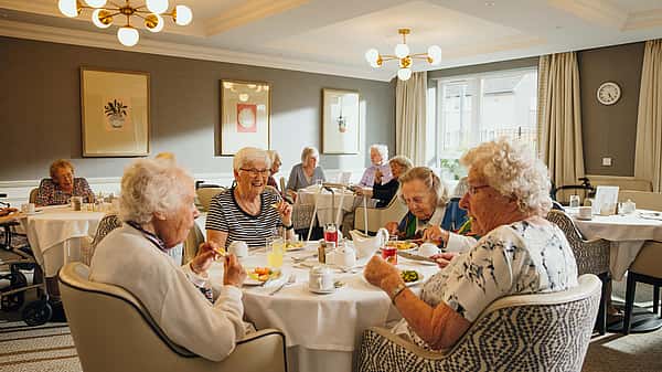 A group of elderly people are enjoying a meal together in a warmly lit dining room