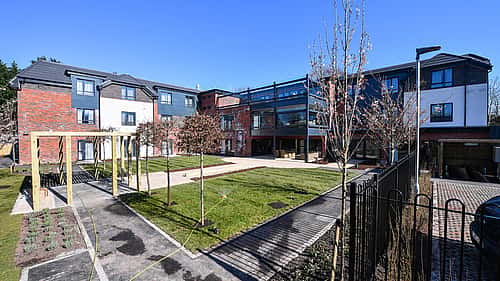 A modern residential building complex with a landscaped courtyard and parking area.
