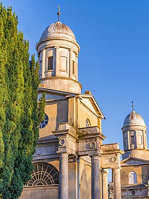 A historic building with twin domes, framed by tall cypress trees, set against a clear blue sky in Essex.