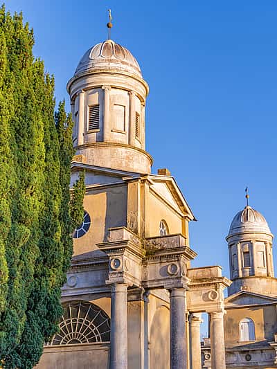 A historic building with twin domes, framed by tall cypress trees, set against a clear blue sky in Essex.