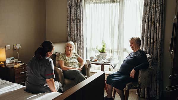 Two elderly women sitting in a cozy room talking to a care professional