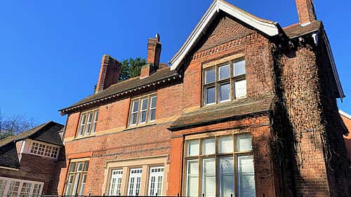 A large, brick house with ivy growing along one side and a clear blue sky above.