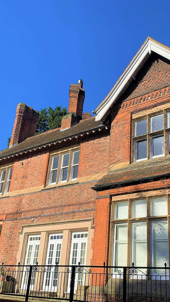 A large, brick house with ivy growing along one side and a clear blue sky above.