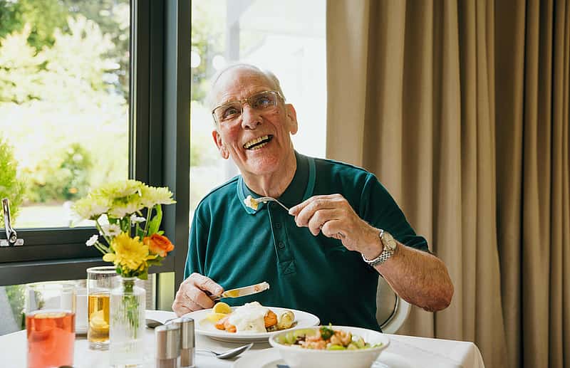 An elderly man dressed in a green shirt enjoying a meal