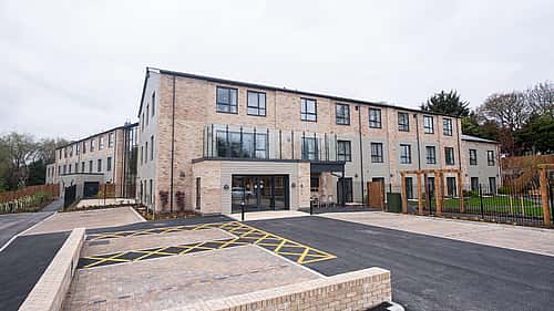 A modern brick building with large windows and a paved parking area in front.