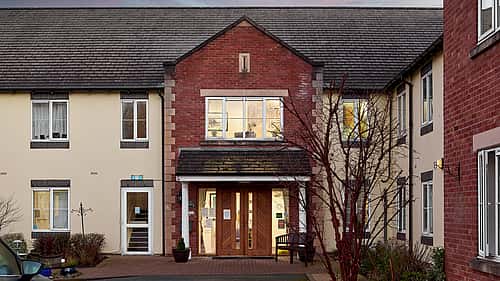 A residential building with a brick facade, featuring a central entrance with large wooden doors and windows on either side.