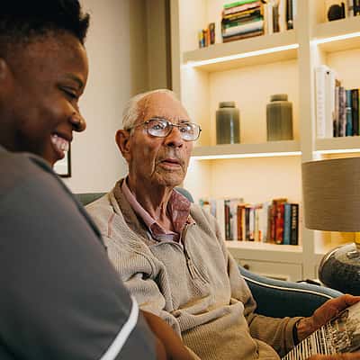 A caregiver and an elderly man smiling while looking at a photo album, surrounded by bookshelves and soft lighting
