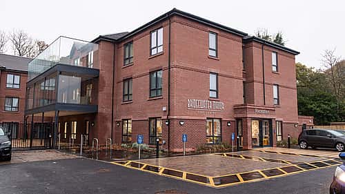 A modern brick building with a glass walkway, parking spaces, and a welcoming entrance.