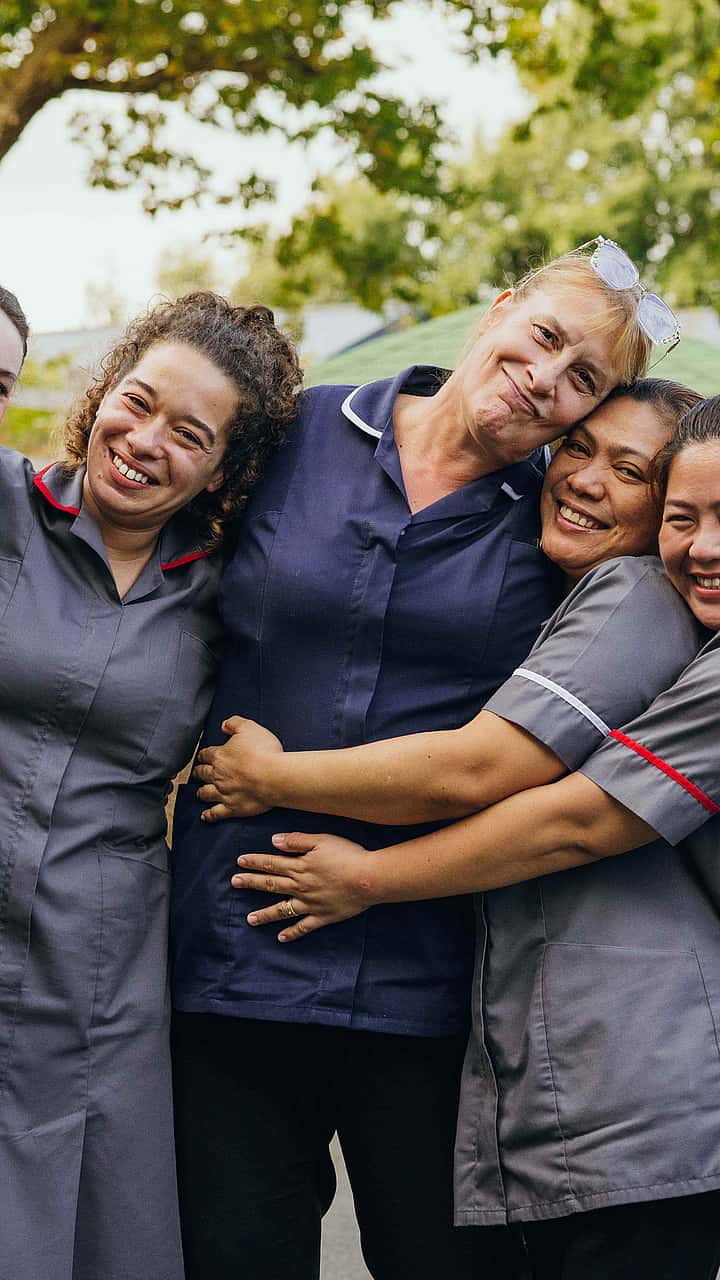 A group of care professionals in grey uniform standing outside in the garden posing for a photograph