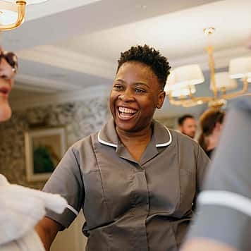 A caregiver smiling and interacting with two elderly individuals, creating a warm and friendly atmosphere