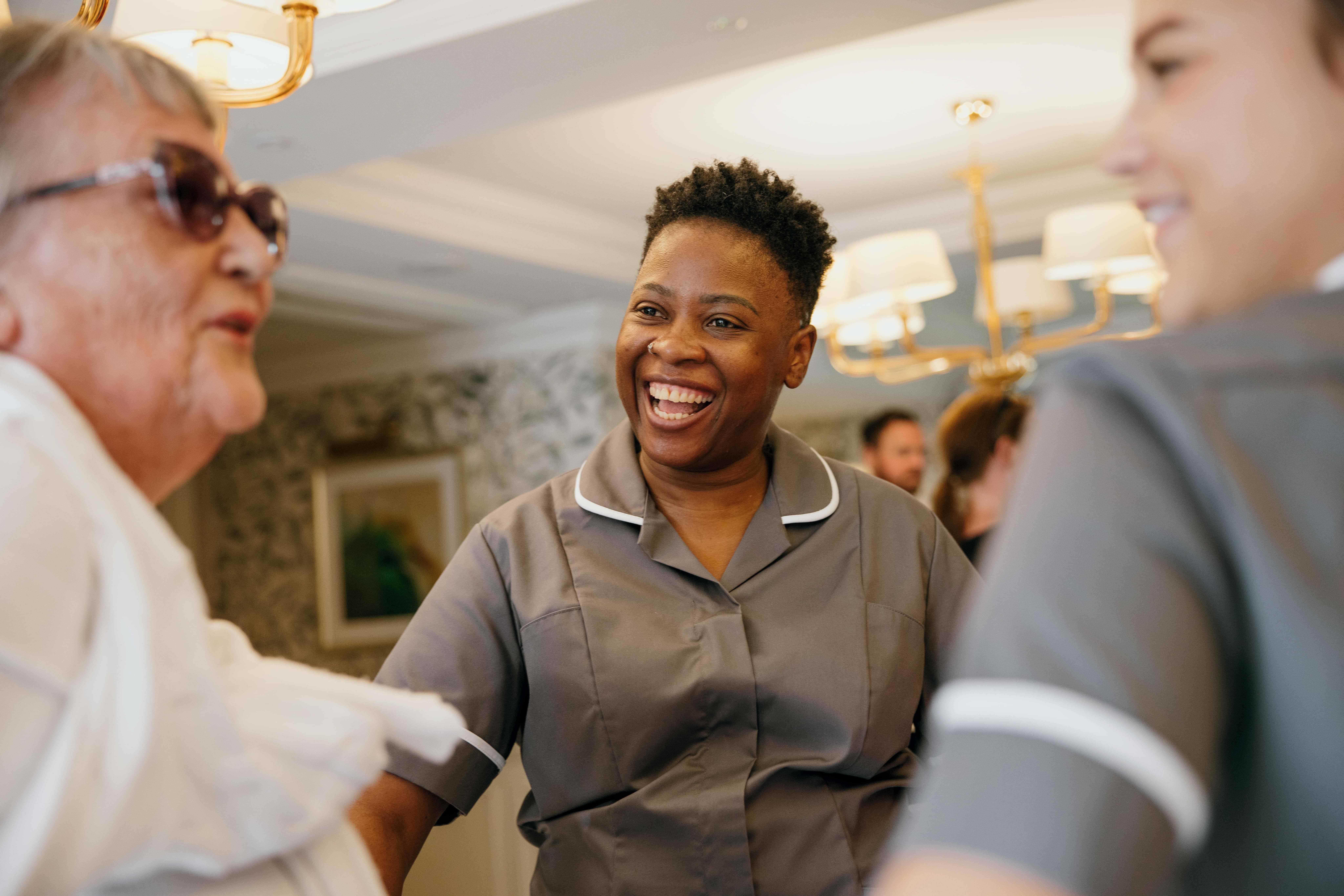 A caregiver smiling and interacting with two elderly individuals, creating a warm and friendly atmosphere