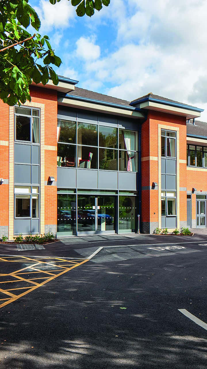A modern two-story building with large windows, surrounded by a well-maintained parking area and greenery.