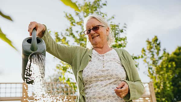 An elderly woman joyfully watering plants in a garden on a sunny day