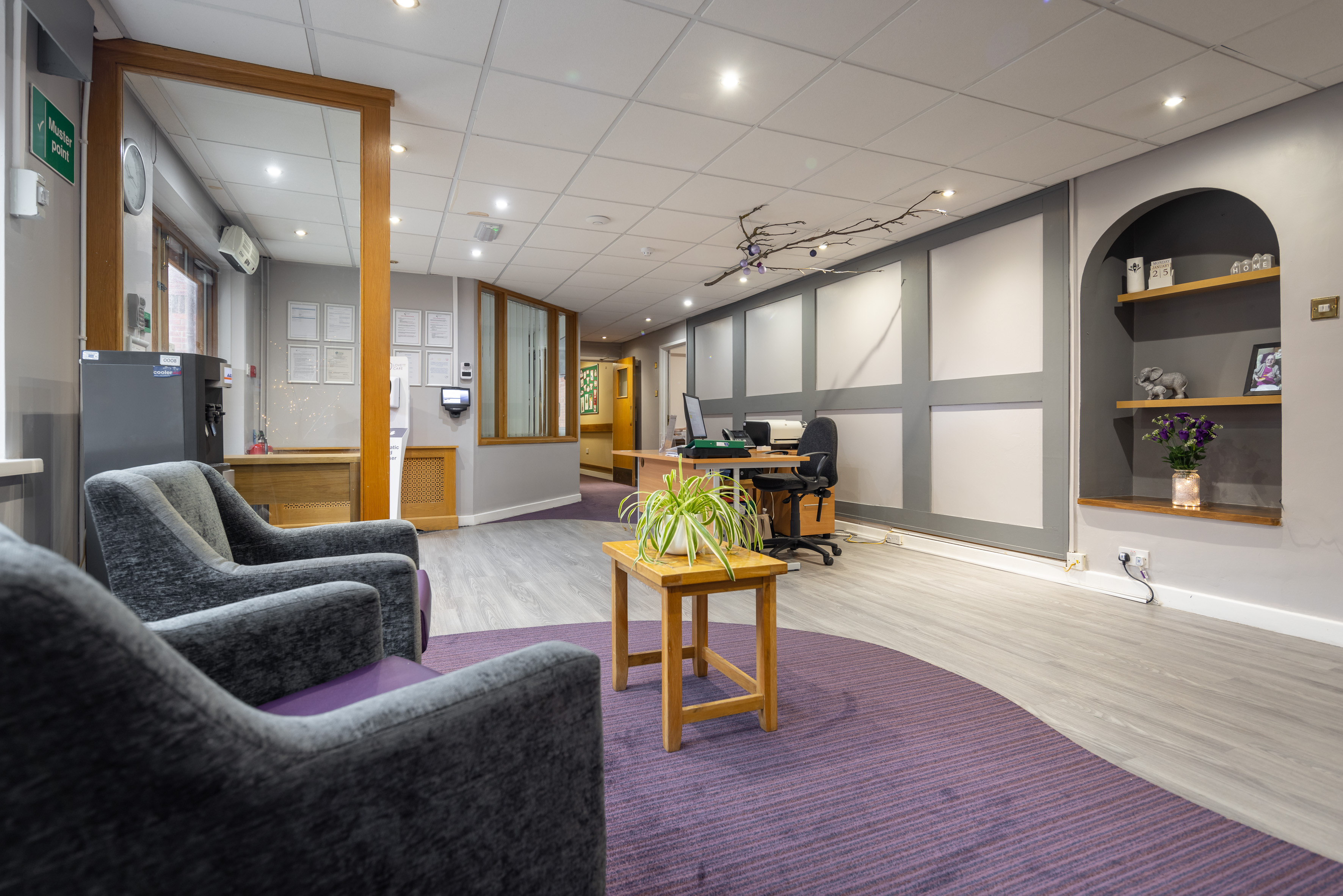 A cozy office waiting area featuring comfortable chairs, a small table, and minimalist shelving on the walls.