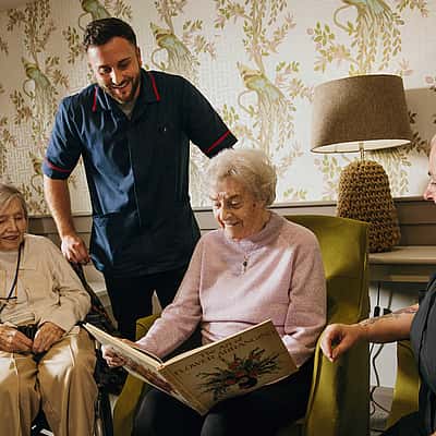 A group of elderly woman viewing a book. Two care professionals giving them company