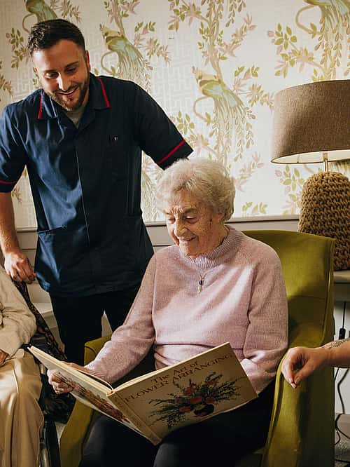 A group of elderly woman viewing a book. Two care professionals giving them company