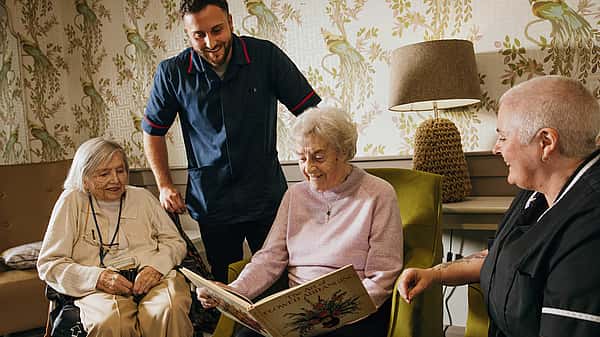 A group of elderly woman viewing a book. Two care professionals giving them company