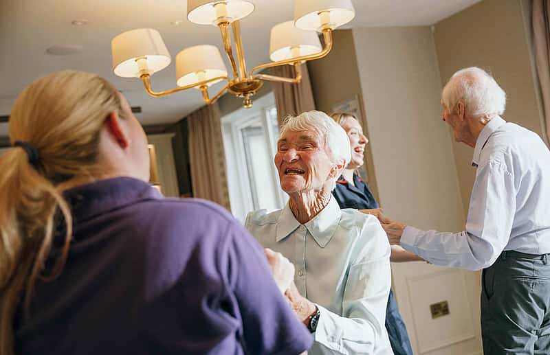 Elderly individuals joyfully dancing with the assistance of caregivers in a well-lit room
