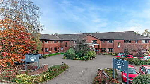 A brick building with a well-maintained parking area, surrounded by autumn trees, featuring signage for "Regency Care Centre.