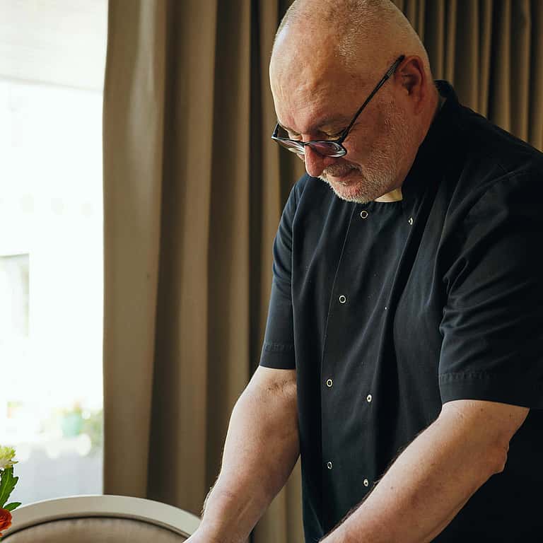 A chef dressed in black setting a meal on the table