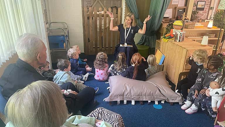 Older adults and young children sit together on the floor for a shared storytelling or group activity in a warm, welcoming room.