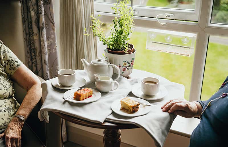 A table with tea and cake with two elderly women seated aside the table.