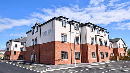 A modern brick-and-white apartment building with spacious parking spaces and clear skies in the background.