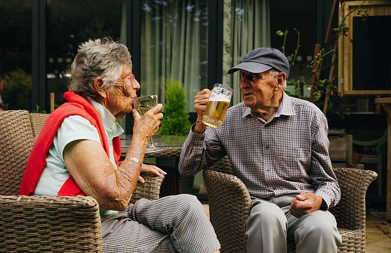Two elderly individuals enjoying a drink in an outside setting.