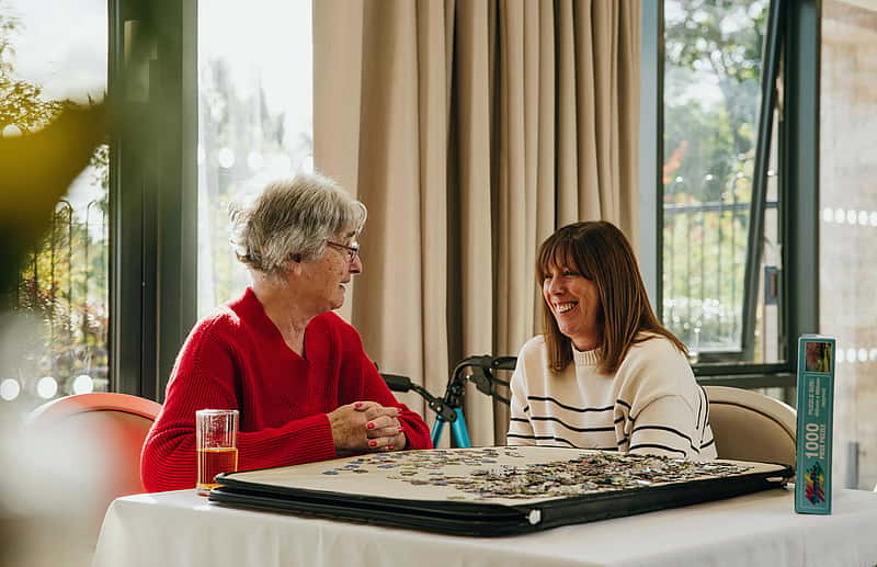Two women have a candid conversation while assembling a puzzle