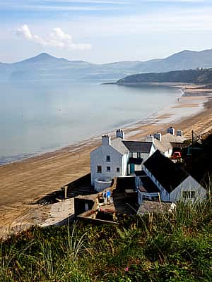 A tranquil beach with sandy shores, bordered by steep cliffs, and overlooking calm waters in North Wales.