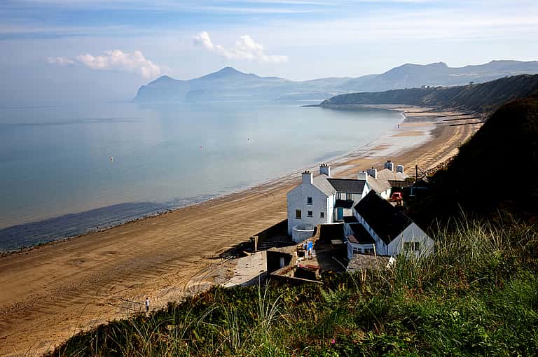 A tranquil beach with sandy shores, bordered by steep cliffs, and overlooking calm waters in North Wales.