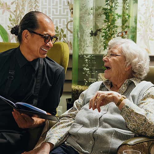 Two individuals conversing, one individual holding an open book in their hands