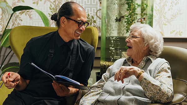 Two individuals conversing, one individual holding an open book in their hands