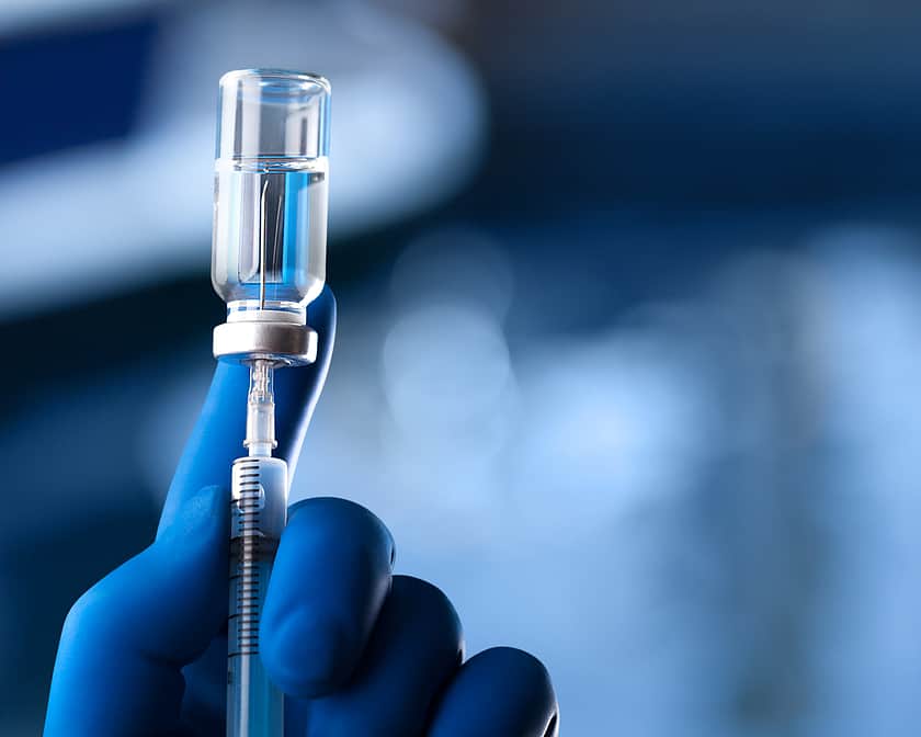 A gloved hand withdrawing liquid from a vial using a syringe.