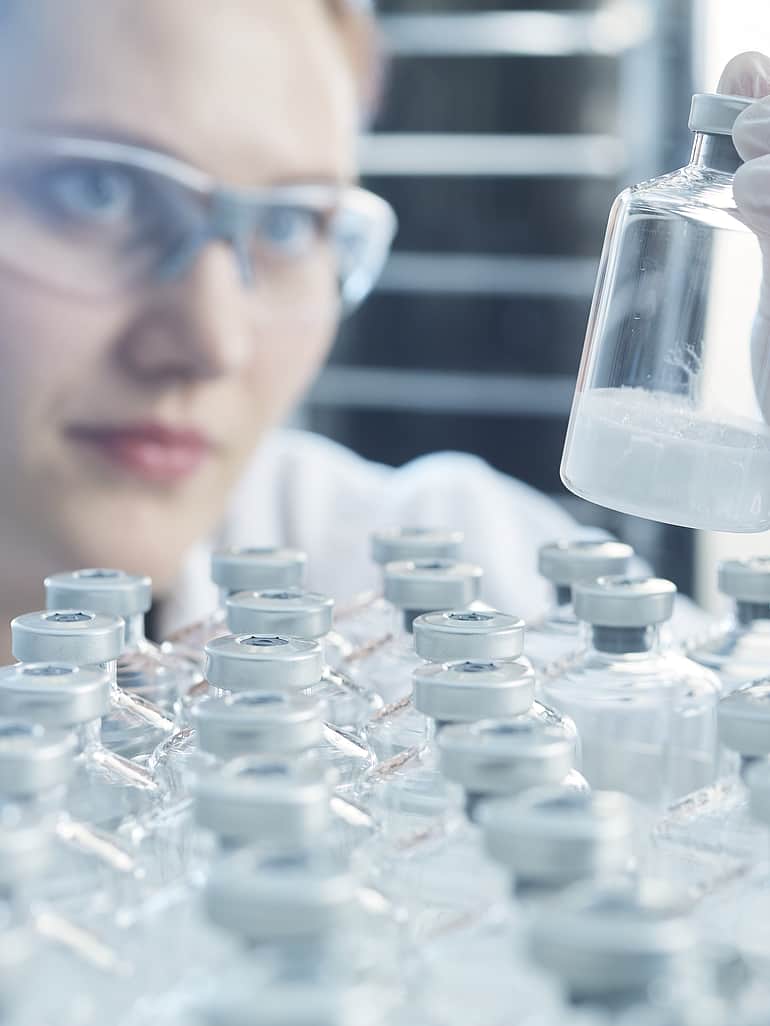 Lab technician inspecting a vial of lyophilized powder.
