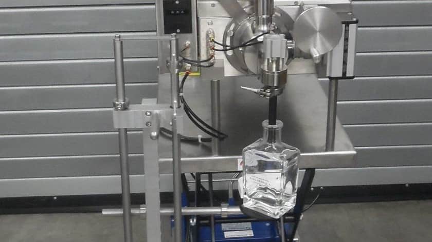 a factory filling machine with the nozzle in the top of a glass whiskey bottle