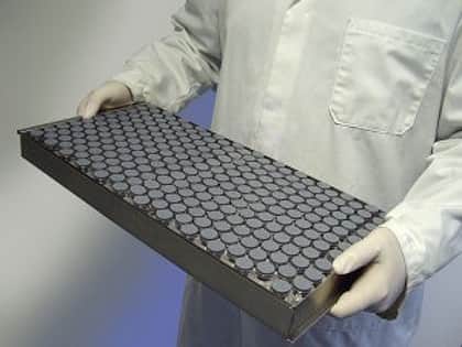 A lab technician holding a metal tray filled with stoppered vials.