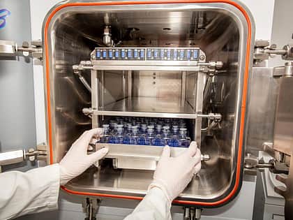 Gloved hands putting a tray of vials into a freeze dryer