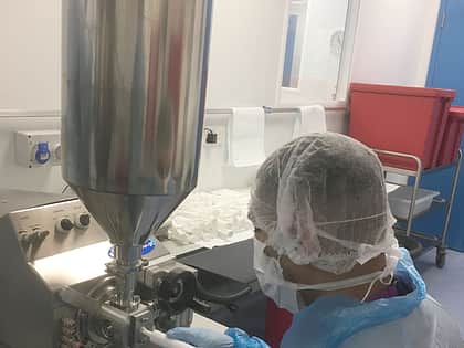 a person with a blue protective overcoat, a hairnet and face mask sits in front of a Response Benchtop filler
