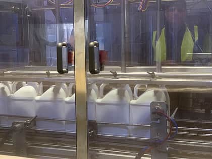 A close up of a line of jerry cans going through a factory filling machine